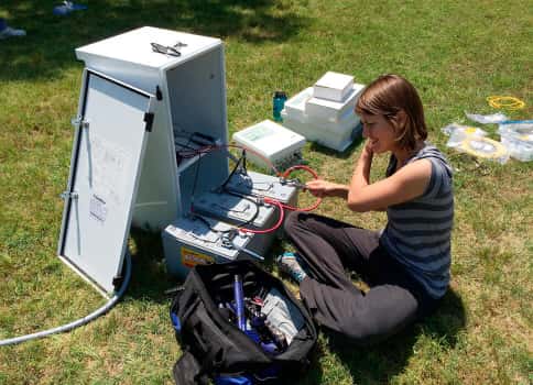 Ph.D. student sitting in grass with meteorological research equipment