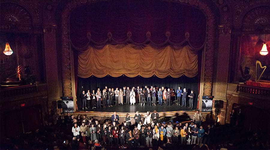 A large group of people stands on and in front of the stage at the Byrd Theatre