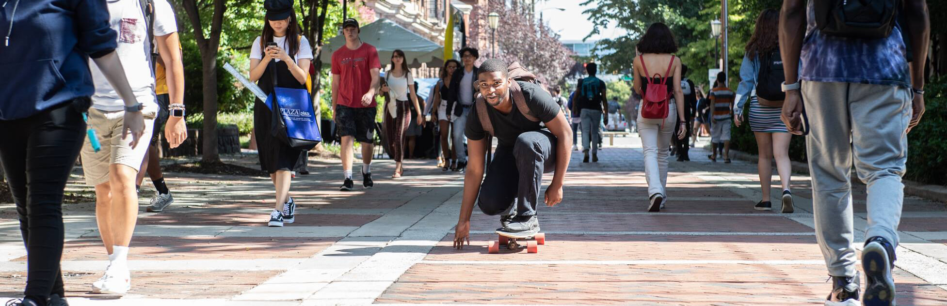 Student skateboarding down a busy walkway.