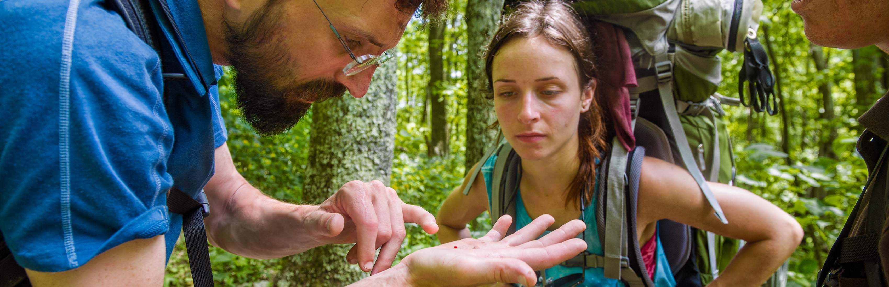 Professor and student examining specimen during nature hike