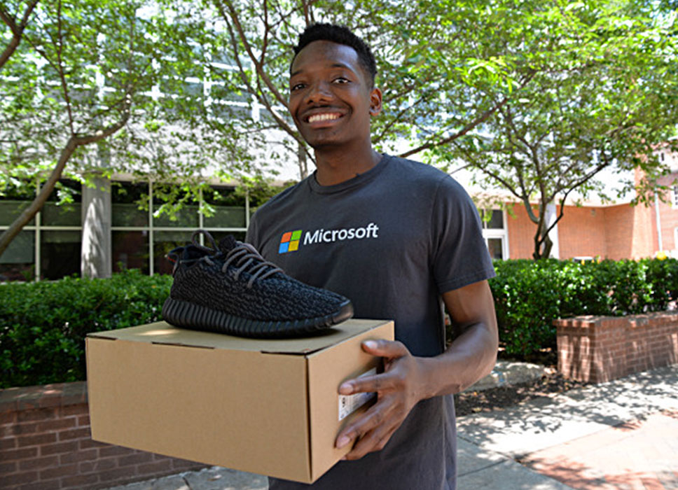 a male student holding a box with a sneaker on top of it